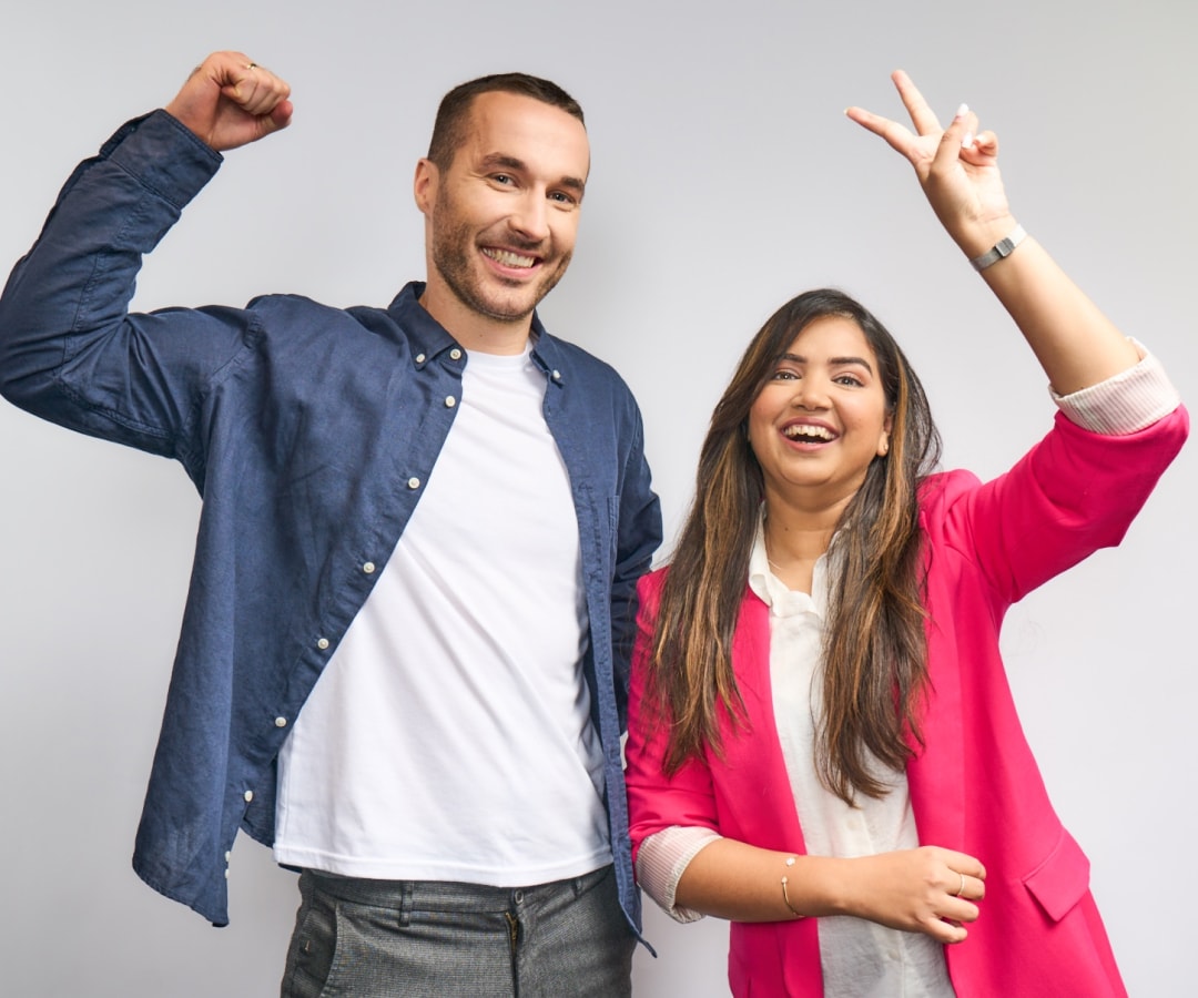 Two Splunkers smile at the camera, each with an arm raised.  One has his hand in a fist, while his colleague shows a peace sign with hers. 