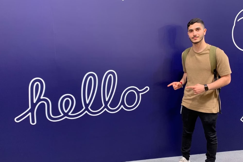  Splunk’s site reliability engineer intern Iliya Dehsarvi says hi by pointing toward a wall with the word “hello” written in cursive.