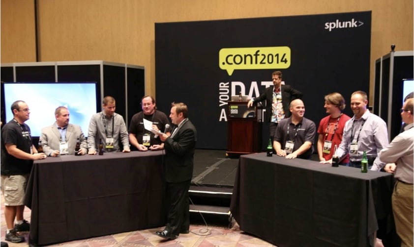 Splunk Revolution Award winners split up into two “families” to play a game of Splunk Family Feud. On the left, Derek Mock, vice president of development at Discovered Intelligence, Greg Hrebek, director of engineering at New York Air Brake, Mikael Bjerkeland, consultant at Datametrix and Richard Griffith, cybersecurity analyst at PNNL listen intently to a question by Jeffery Blake, Splunk's very own Richard Dawson. Behind him stands Maverick Garner, Director of all thy Splunk sales engineers.