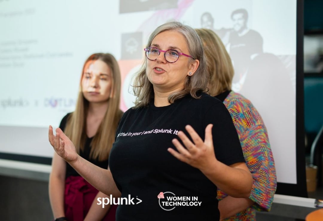 A Splunker gesturing while delivering a presentation. Two Splunker teammates and her slide deck appear in the background.