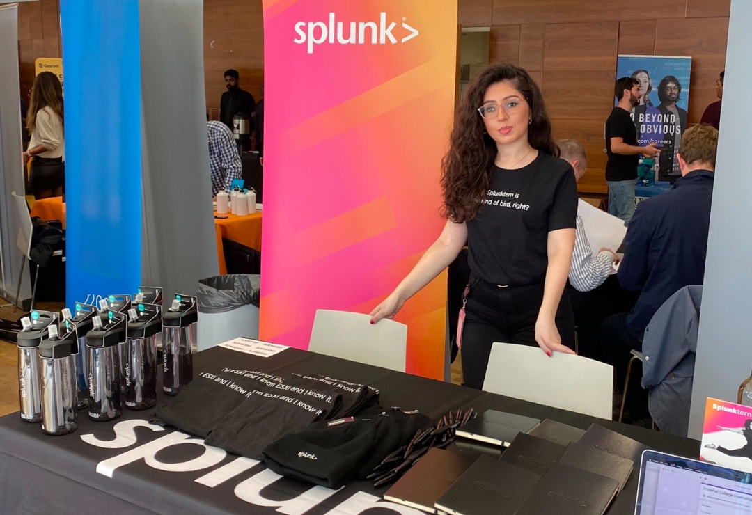 A Splunker attending a recruiting event. She is standing at a table filled with Splunk water bottles and t-shirts.