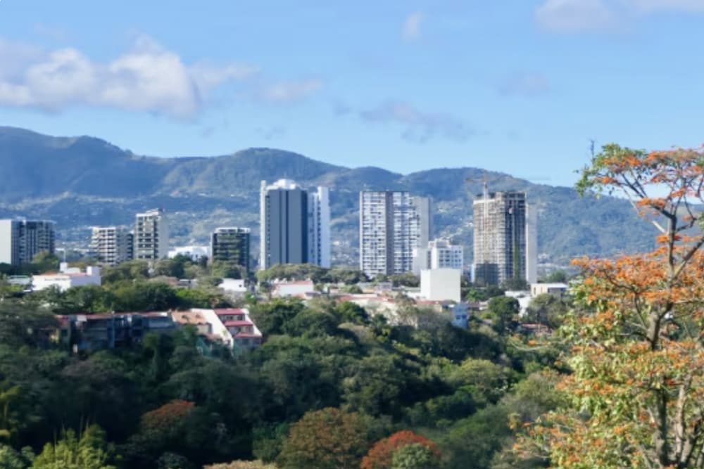 Eine Gruppe von hohen Gebäuden auf einem bewaldeten Plateau mit einer Bergkette und Wolken in der Ferne. Splunk hat ein Büro in San José, Costa Rica.