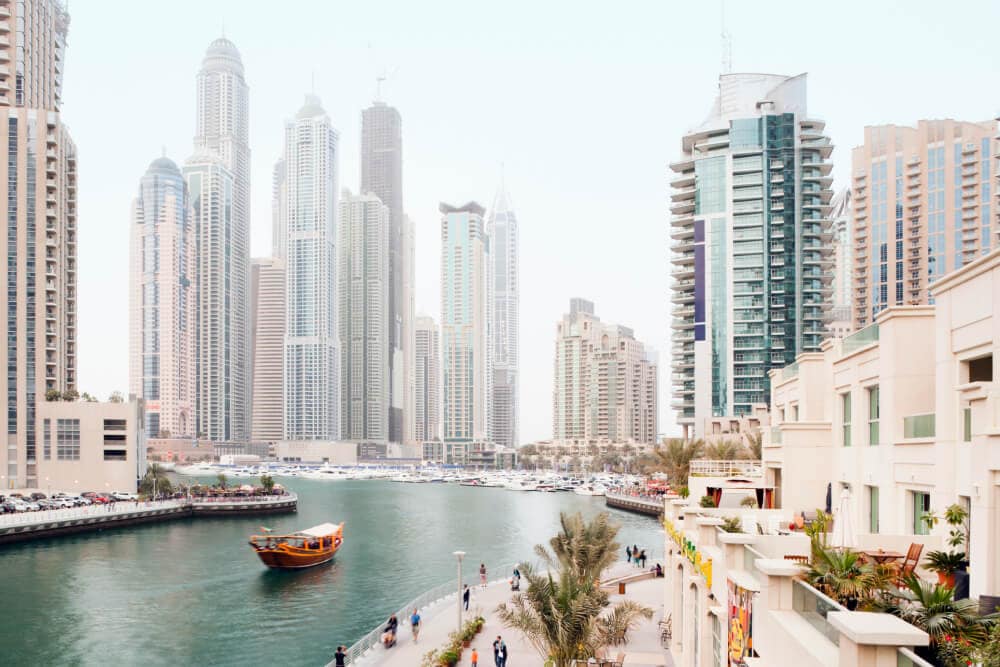 A canal runs through a busy urban area, with massive skyscrapers in the distance giving way to smaller beige buildings and a tree-lined promenade in front. Splunk has an office in Dubai, United Arab Emirates. 