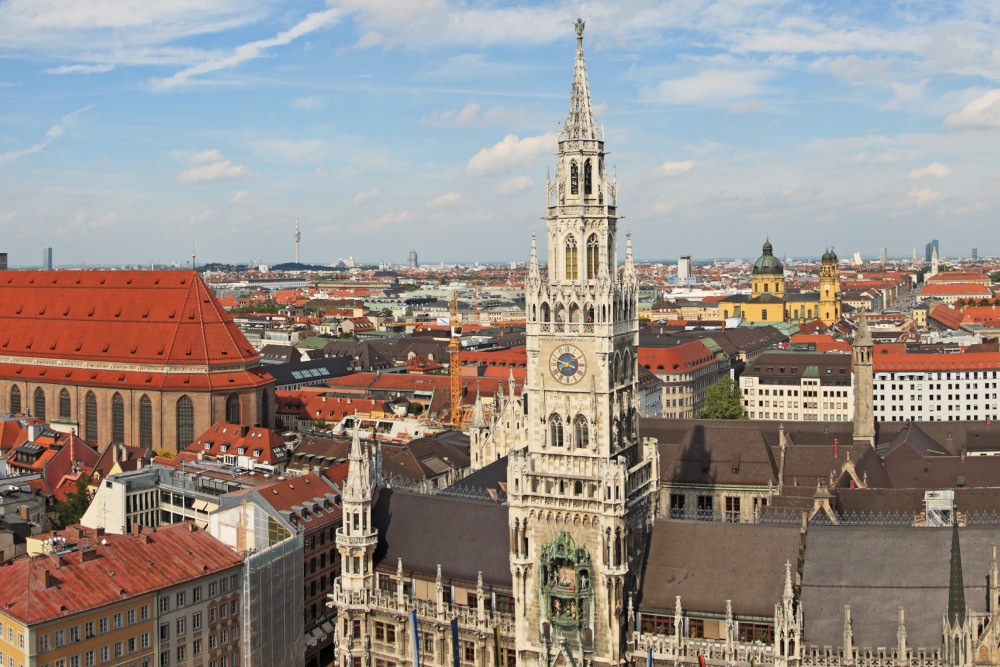 Ein hoher beiger Glockenturm erhebt sich über einer dichten Gruppe von Gebäuden mit roten Dächern in München, wo Splunk ein Büro hat.