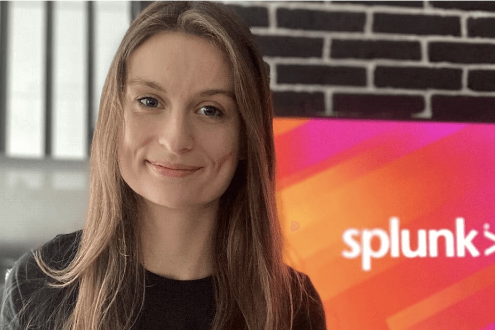 A Splunker working in Krakow smiles in front of a monitor displaying the Splunk logo.