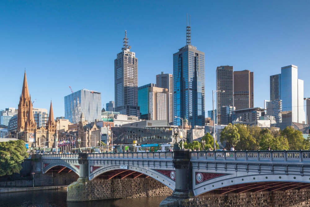 Dunkle Wolkenkratzer überragen eine niedrige Brücke, die einen Kanal überspannt. Braune Kirchtürme sind am anderen Ende der Brücke in Melbourne, Australien, zu sehen, wo Splunk ein Büro hat.