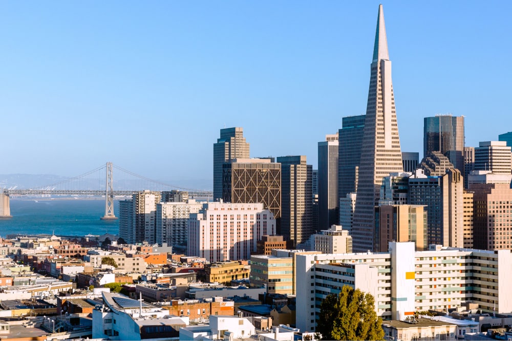 Die hohe Transamerica Pyramid überragt eine Ansammlung von Wolkenkratzern im Geschäftsviertel von San Francisco. Im Hintergrund sieht man die Bay Bridge. Splunk hat ein Büro in San Francisco, Kalifornien.