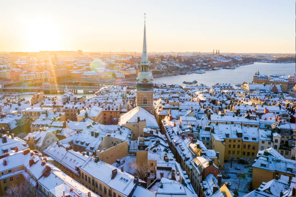 Ein hoher, spitzer, grüner Glockenturm überragt eine Gruppe niedriger, schneebedeckter Gebäude in Stockholm, wo Splunk ein Büro hat.