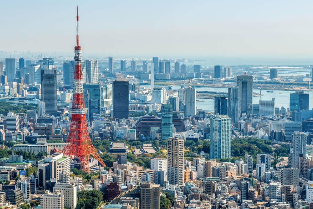 Ein rot-weißes Bauwerk, das wie der Eiffelturm aussieht, bildet einen Kontrast zu den blauen und silbernen Geschäftsgebäuden und dem fernen Meer in Tokio, Japan, wo Splunk ein Büro hat.