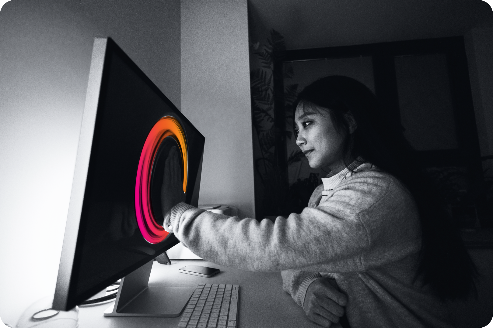 A women sitting on her desk, places her palm on a monitor while a circle gradient encompasses it. 